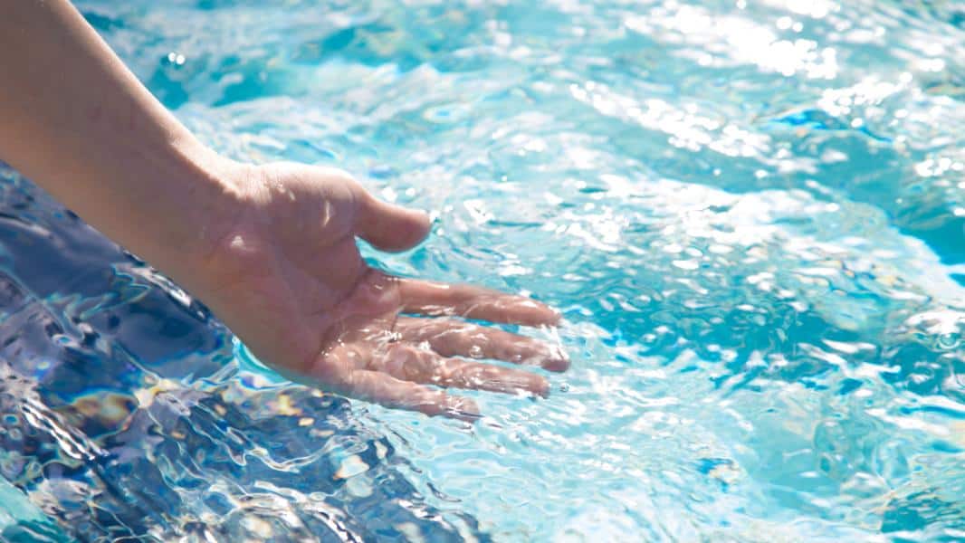 a hand runs through clear and clean pool water treated by a UV sanitizer system