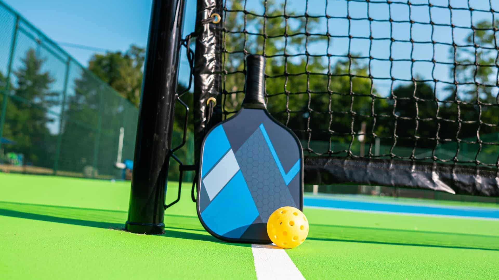 An outdoor pickleball court with a net, paddle, and ball